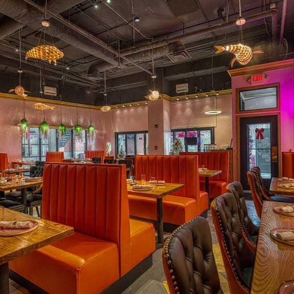Restaurant interior with orange booths, wooden tables, pink walls, and fish-shaped ceiling lights.