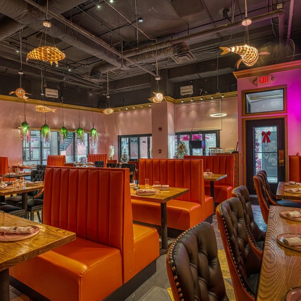 Vibrant restaurant interior with orange booths, wooden tables, pink walls, and unique fish-shaped light fixtures.