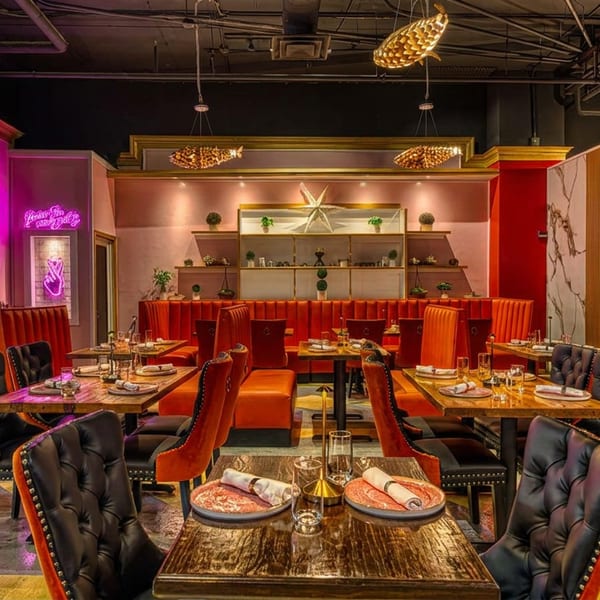 Vibrant restaurant interior with orange booths, black chairs, pink walls, and golden fish light fixtures.