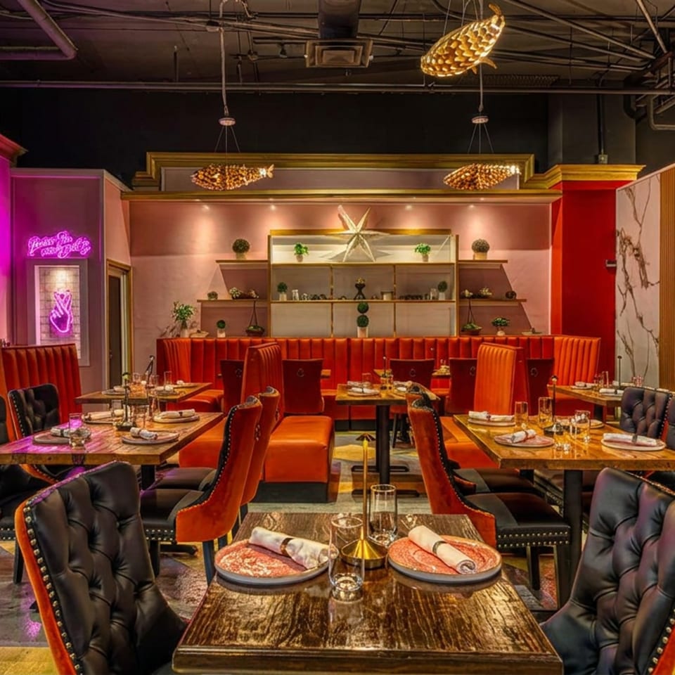 Vibrant restaurant interior with orange booths, black chairs, pink walls, and golden fish light fixtures.