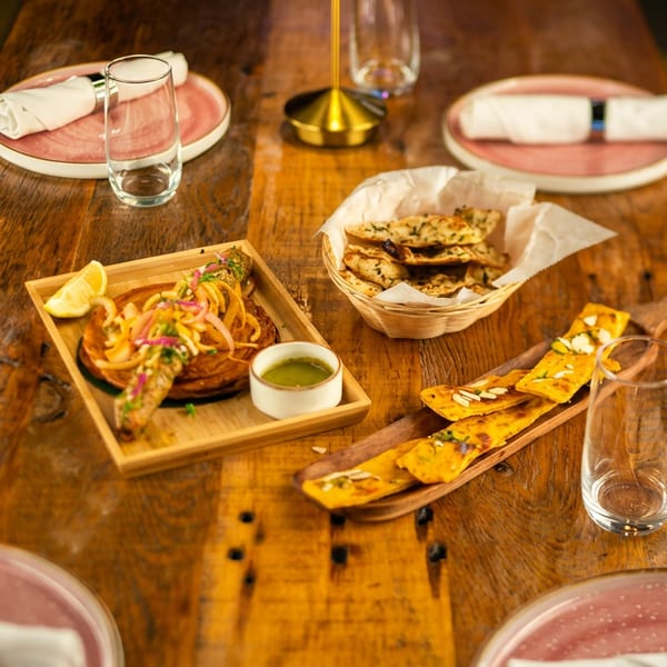 Assortment of Indian dishes including kebab, flatbreads, and chutneys on a rustic wooden table.