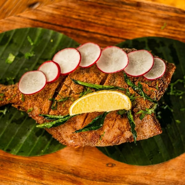 Crispy fried fish garnished with radish, lemon, and herbs, served on banana leaves with green sauce.
