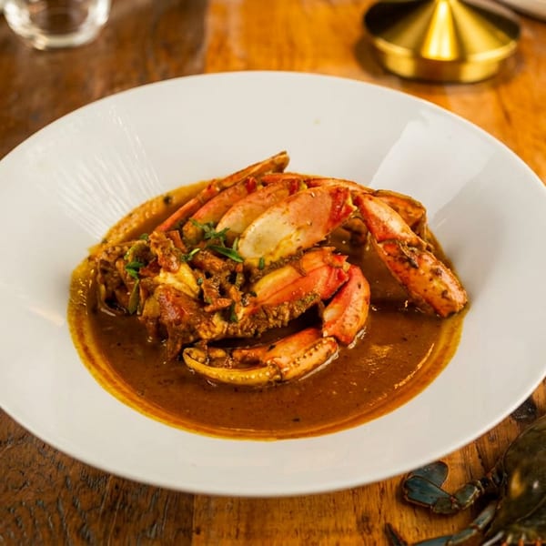 Cooked crab in a rich sauce on a white plate, with a raw crab on a wooden table.