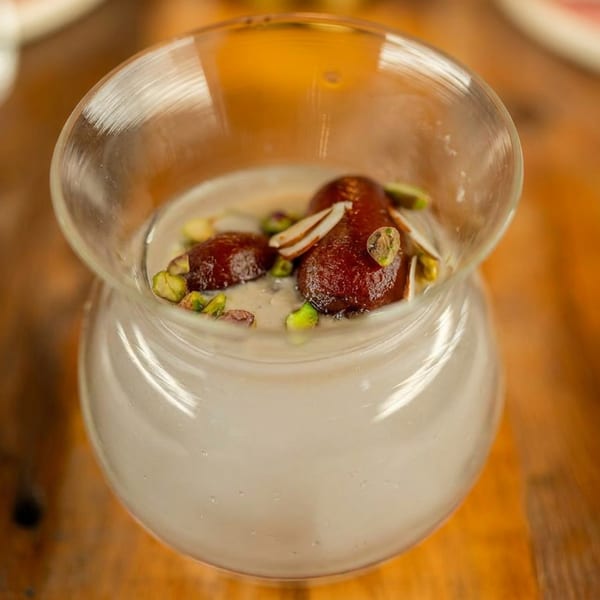 Creamy dessert with Gulab Jamun, pistachios, and almonds in a clear glass.