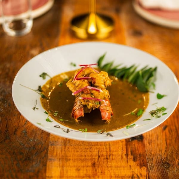 Lobster tail in a golden sauce, garnished with red strips and green herbs, served on a wooden table.